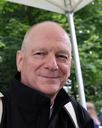 Photo de Jean-Claude Tarby, souriant, vêtu d'une chemise blanche, dans un bureau universitaire